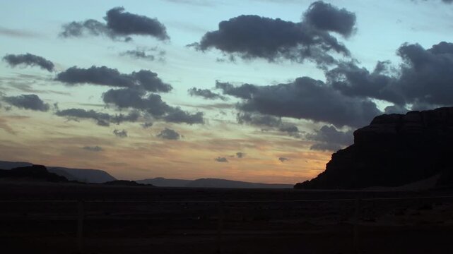 Cinematic sunrise timelapse over the red sand and rock formations of Wadi Rum, Jordan. Sun rising behind desert mountains, illuminating the iconic landscape of the Valley of the Moon