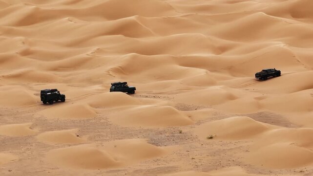 High angle drone shot of three 4x4 overland vehicles crossing soft sand dunes in the Tunisian Sahara. off-road expedition navigating the remote desert landscape of North Africa
