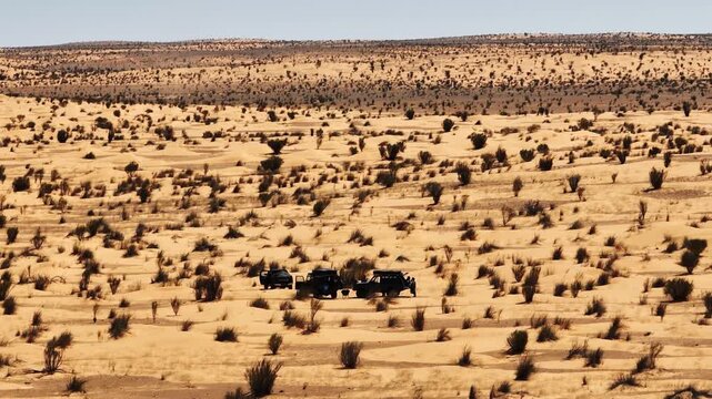 Aerial view of an overland basecamp with 4x4 vehicles in the Sahara Desert, Tunisia. Travelers camping among dunes and shrubs during an off-road expedition in the North African wilderness