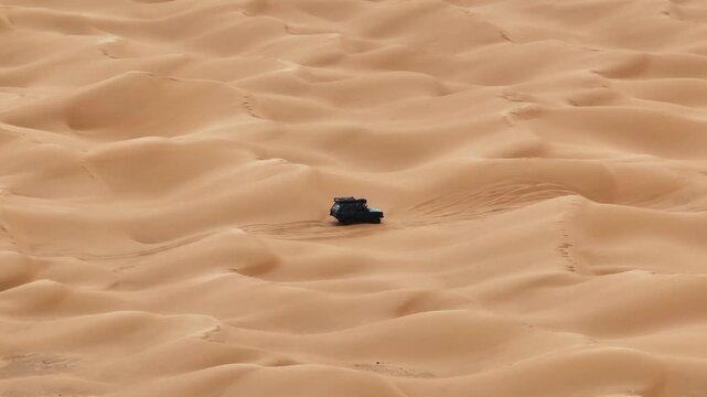 Aerial drone view of a dark Range Rover Classic driving solo across the vast sand dunes of the Sahara Desert in Tunisia. Professional overland expedition and off-road adventure travel