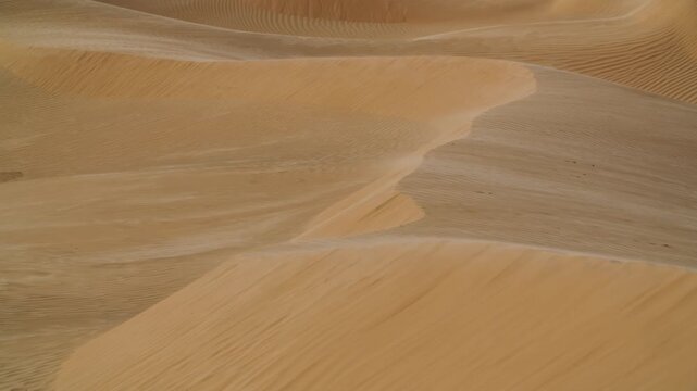 Close-up static shot of sand blowing off the sharp crest of a desert dune in Tunisia. Natural wind patterns and sand movement in the Sahara Desert under bright daylight conditions