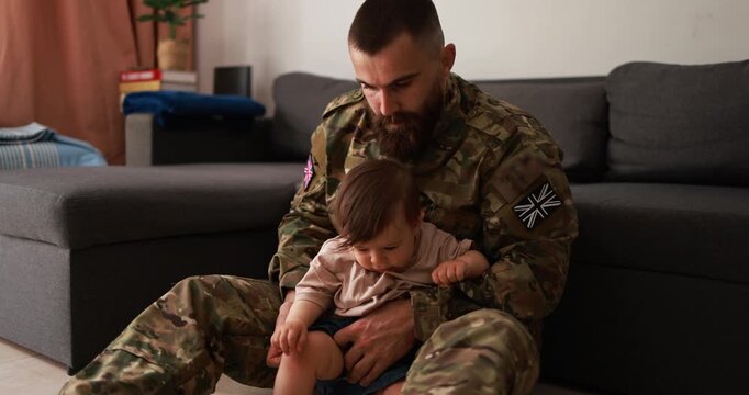 English male soldier in military uniform having playful time with his little son at home - Emotional military happy homecoming concept
