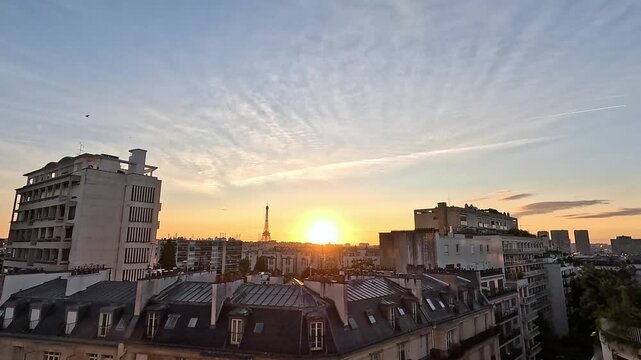 Timelapse of a golden sunrise over the Paris skyline with the Eiffel Tower silhouetted against a warm glowing sky. Filmed from a rooftop overlooking Haussmann buildings and city rooftops on a clear mo