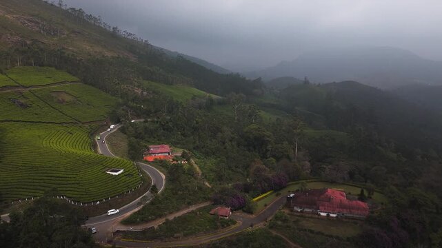 Aerial rising shot of winding mountain road and tea gardens in rainy Munnar, India