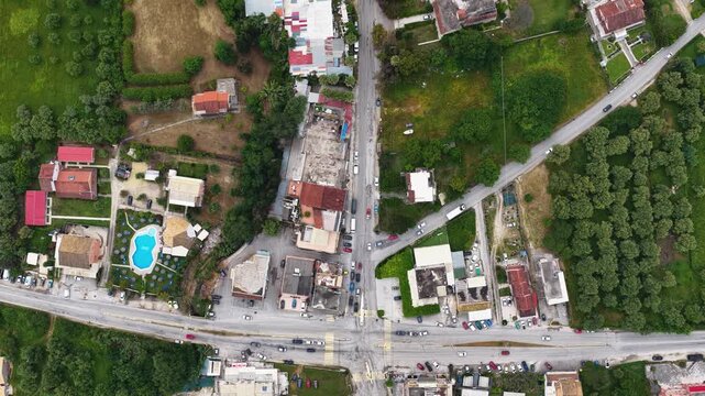 Aerial overhead drone view of a rural crossroad intersection with car traffic, houses, and green nature in Roda village, North Corfu, Greece. Beautiful bird's-eye perspective of summer travel.