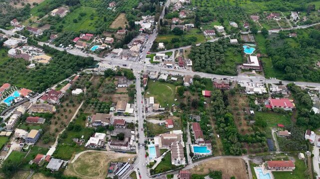 Aerial drone shot of Roda resort town in North Corfu featuring a main road intersection, villas, and countryside.
