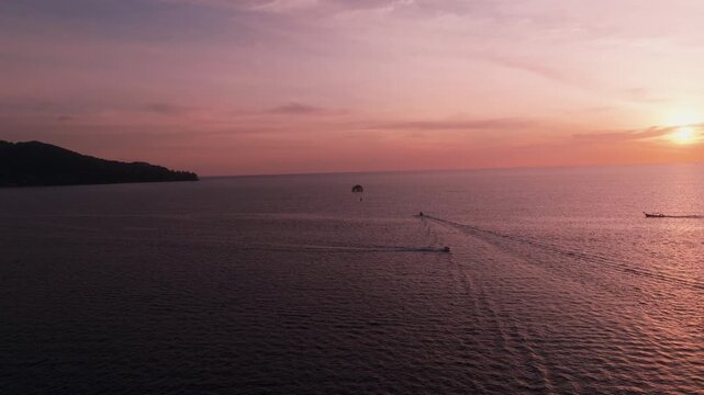 Drone follows boats and parasailing over sea at sunset in Phuket