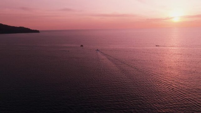 Drone following parasailing boat over sea with pink sunset sky