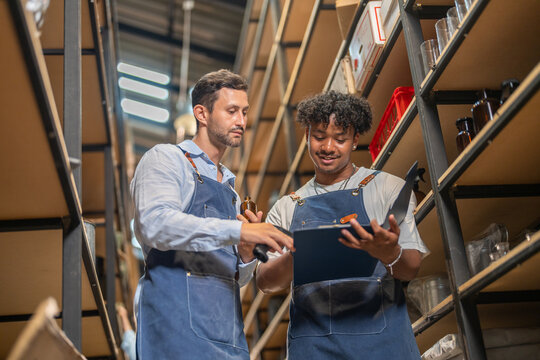Two diverse male workers in aprons checking inventory with barcode scanner and clipboard in small business warehouse, Teamwork, retail stock management, logistics, e-commerce supply chain, partners
