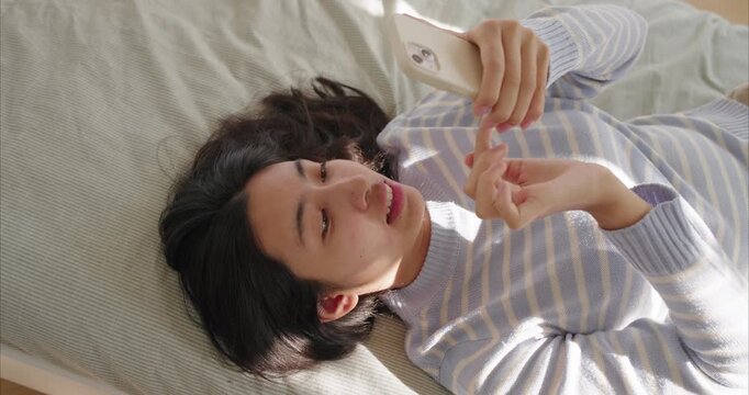 Happy asian teenage girl lying near on bed, using smartphone, Top view