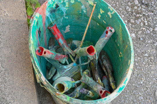 A bucket full of paint rollers and brushes. Preparations for painting or decorating a wall. Wall rollers and brushes of various sizes. Brushes and rollers full of paint.