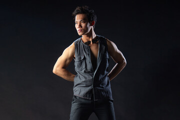 Obraz premium A stylish Asian man in sleeveless casual places both hands behind him while looking away from the camera, sunglasses hanging on his neck, creating a relaxed and stylish silhouette.
