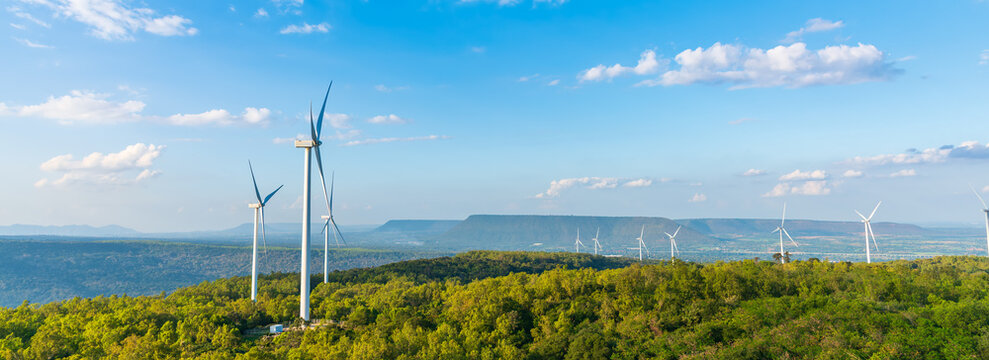 Panoramic view of a large wind farm with turbines on green hills. Renewable energy production and clean technology landscape under blue sky with clouds.