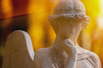 Fototapeta premium Thoughtful angel statue with hand near lips in warm golden sunlight, symbolic image of silence, contemplation and spiritual mystery