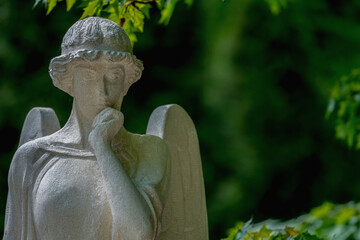 Fototapeta premium Thoughtful angel statue in peaceful green cemetery atmosphere
