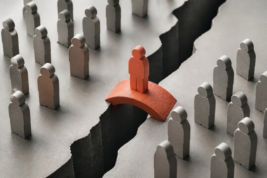 Orange figure crossing a bridge over a gap among gray paper people with copy space for business concept