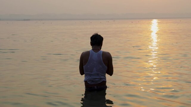 man performing morning prayer in ganges river during peaceful sunrise at varanasi chhath festival