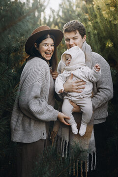 Happy family hugging with cute baby son in autumn woods in soft evening light. Parenthood. Mother father and little child in cozy stylish clothes smiling in fall park