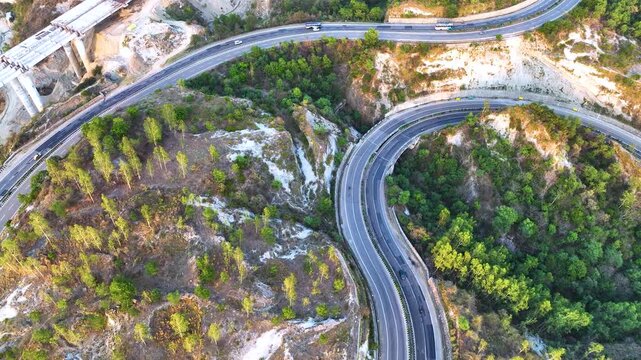 Top-down aerial drone footage capturing transport trucks and commuter vehicles navigating a sweeping S-curve on a major national highway.