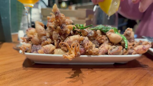 Closeup view of a plate plenty of Andalusian style fried calamari, with a view of a woman hand squeezing lemon-