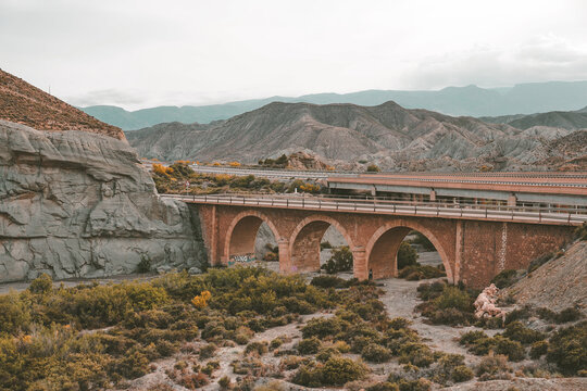 Historic stone viaduct and modern highway crossing the arid mountains of Tabernas Desert, Almeria, Spain. Travel and transport concept.
