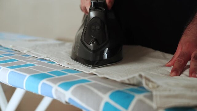 Ironing white garment on patterned board using modern steam iron