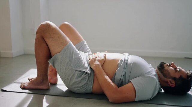 Starting breathing, man in grey t-shirt doing pelvic tilt on dark mat in studio for core