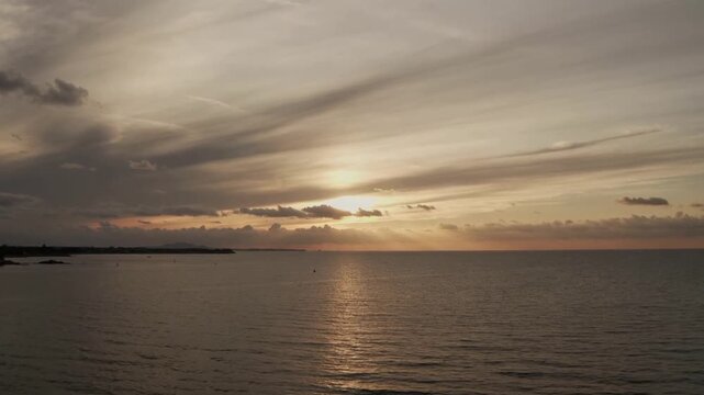 Nearing horizon, sun descending and casting vertical reflection over calm sea from shore, buoy