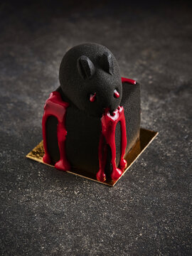 The image showcases a black dessert cake designed in the shape of a bear, featuring vibrant red sauce dripping from it