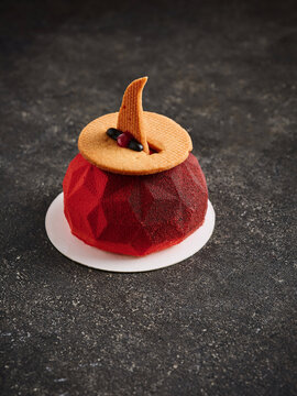 This image showcases a red mousse dessert topped with a cookie garnish and decorative elements. It is ideal for use in dessert menus, fine dining advertising, and upscale culinary promotions