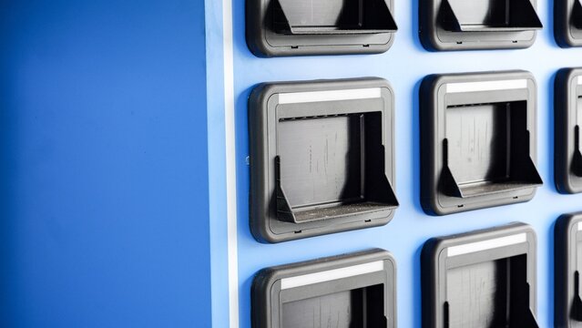 Close-up of a blue automated vending or battery swapping station featuring rows of black plastic dispensing slots with protective hoods, highlighting modern convenience infrastructure.