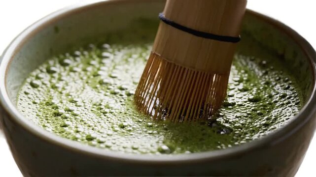Close-up of a bamboo whisk stirring vibrant green matcha tea in a traditional bowl.