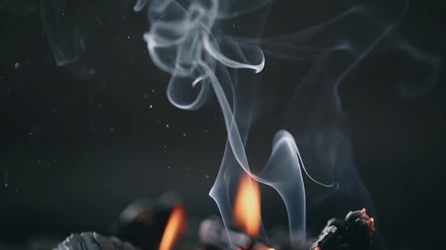 Glowing embers and flame releasing smoke in fire pit over charred wood, heat feeding sparks