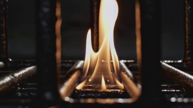 Sparking electrode igniting, gas flame rising from burner head on stovetop, showing cast-iron grate