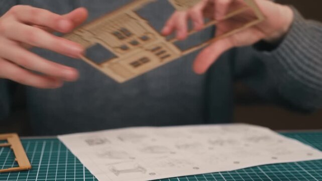 Removing roof and wall pieces from wooden model template. DIY house assembly concept, hands preparing miniature construction parts. Architectural crafting process, hobby maker project