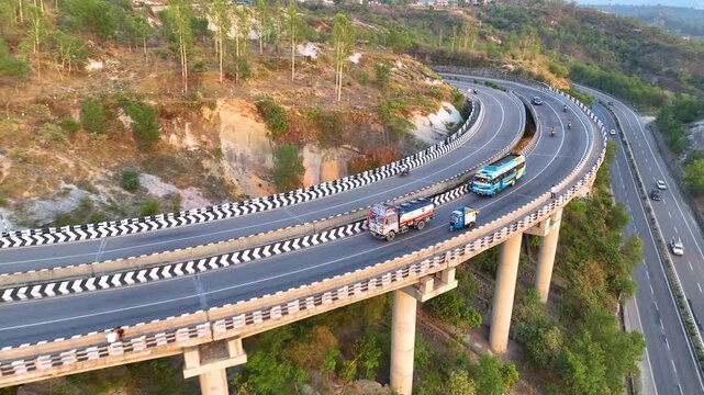 Freight truck driving on elevated highway curve. Cinematic aerial side-tracking footage following a brightly colored commercial transport truck as it navigates a sweeping, elevated curve on highway