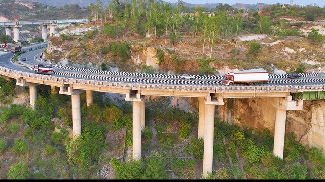 Freight truck driving on elevated highway curve. Cinematic aerial side-tracking footage following a brightly colored commercial transport truck as it navigates a sweeping, elevated curve on highway