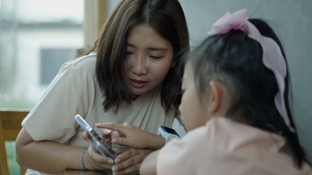 Adult woman teaching young girl using smartphone, digital learning concept