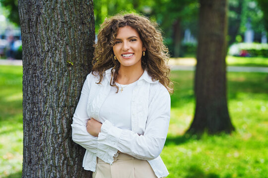 A businesswoman leaning against a tree in the park in the summer sunlight.