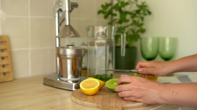 Female hands cutting lemons and limes in half with a knife for homemade lemonade. Cold summer drink