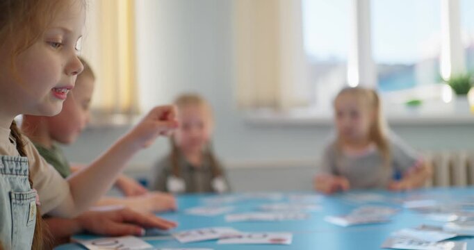 Young children gather around a classroom table sorting picture cards during a bright group learning activity with teacher guidance