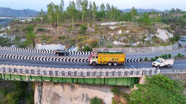 Freight truck driving on elevated highway curve. Cinematic aerial side-tracking footage following a brightly colored commercial transport truck as it navigates a sweeping, elevated curve on highway