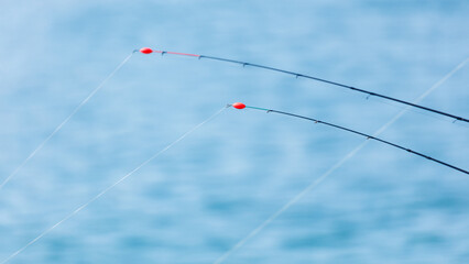 Fishing rods with red floats against serene blue water background © schankz
