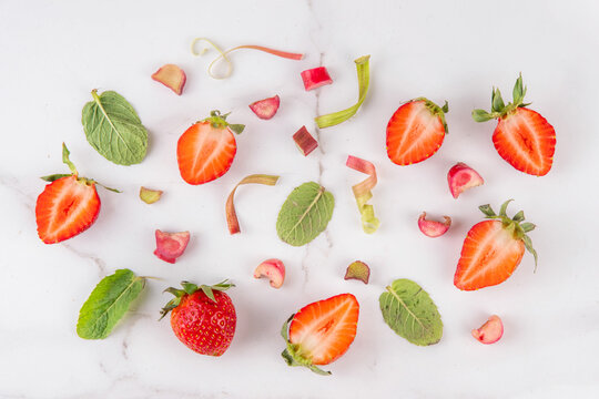 Strawberry Rhubarb and Mint Flat Lay pattern background. Slices of strawberry, Rhubarb stems, Mint lay out on a white marble table, top view, copy space