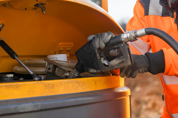 Person fuels machinery at a construction site during daylight hours in an outdoor setting © Iryna