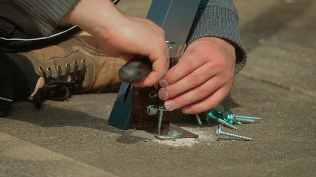 Socket wrench tightening screw into anchor embedded in concrete foundation detail. Worker fastening metal support plate with hardware for secure load bearing connection. Construction assembly concept