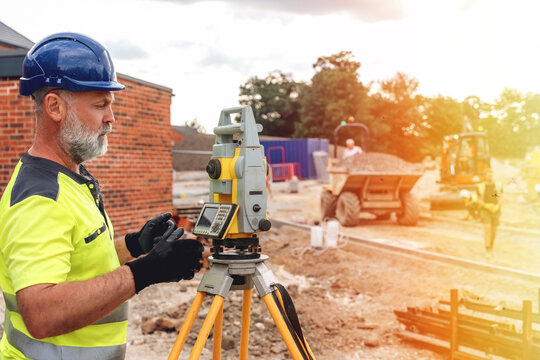 Construction worker uses a survey instrument to measure land during a project at a site in the afternoon light in a city