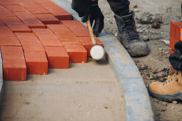 Workers lay bricks on a construction site during daytime to create a pathway or surface for pedestrians and vehicles © Iryna
