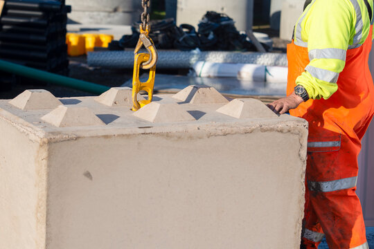 Worker lifts concrete block at construction site using a crane in bright daylight