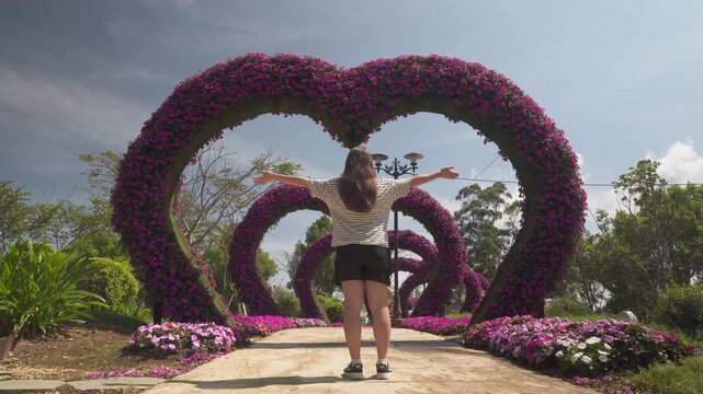 Woman is opening her arms under heart-like flower arch